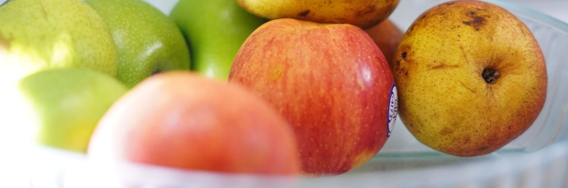 Vibrant apples and pears arranged in a clear bowl, showcasing freshness against a soft background.